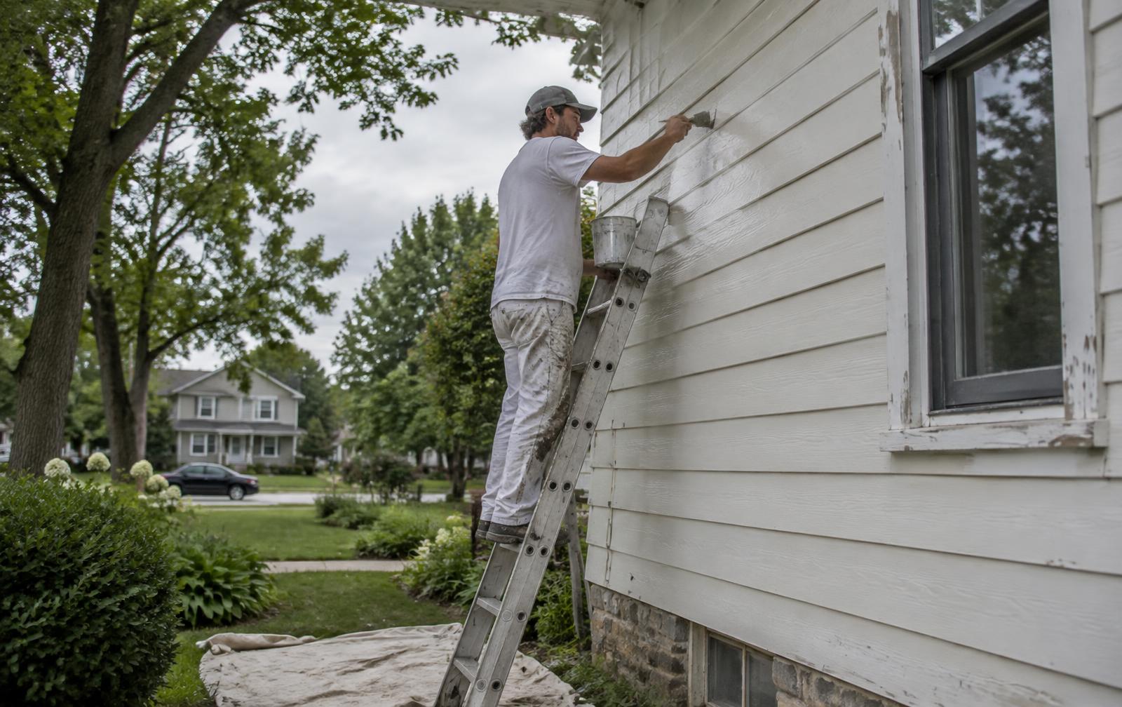 Painter applying a fresh coat to exterior house siding from a ladder
